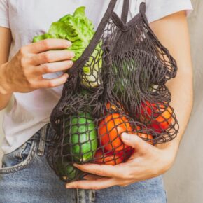 Girl holding mesh shopping bag full of vegetables and taking from inside a fresh lettuce from the farm. Sustainable, zero waste and plastic free lifestyle. Save the planet concept